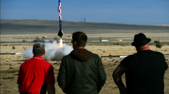 Model rocket takes off as Allen Haff and Ton Jones watch nearby.